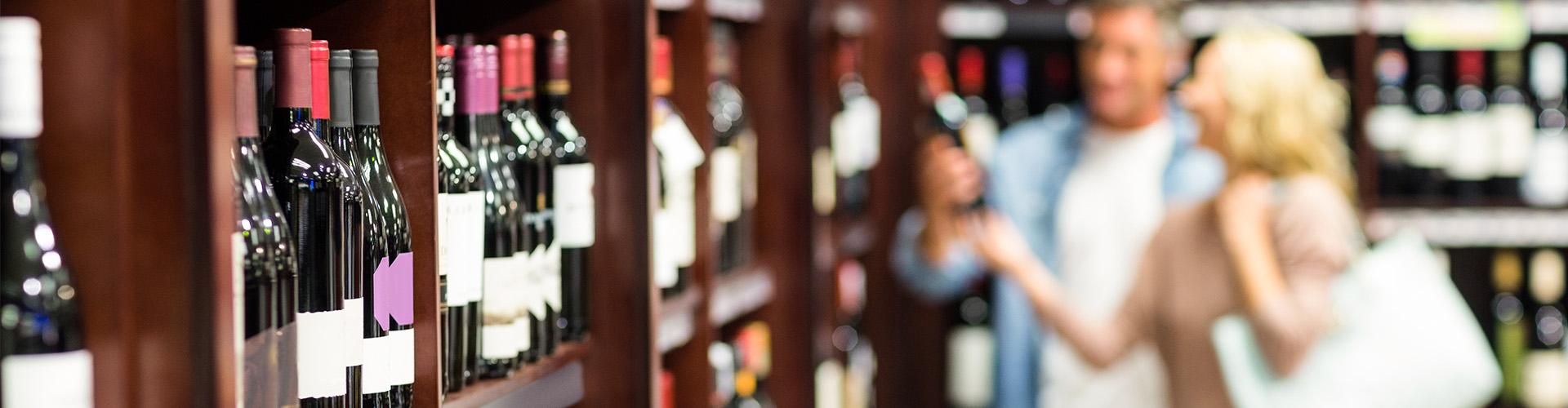 Une boutique remplie de bouteilles où deux clients observent attentivement un vin chez un caviste.